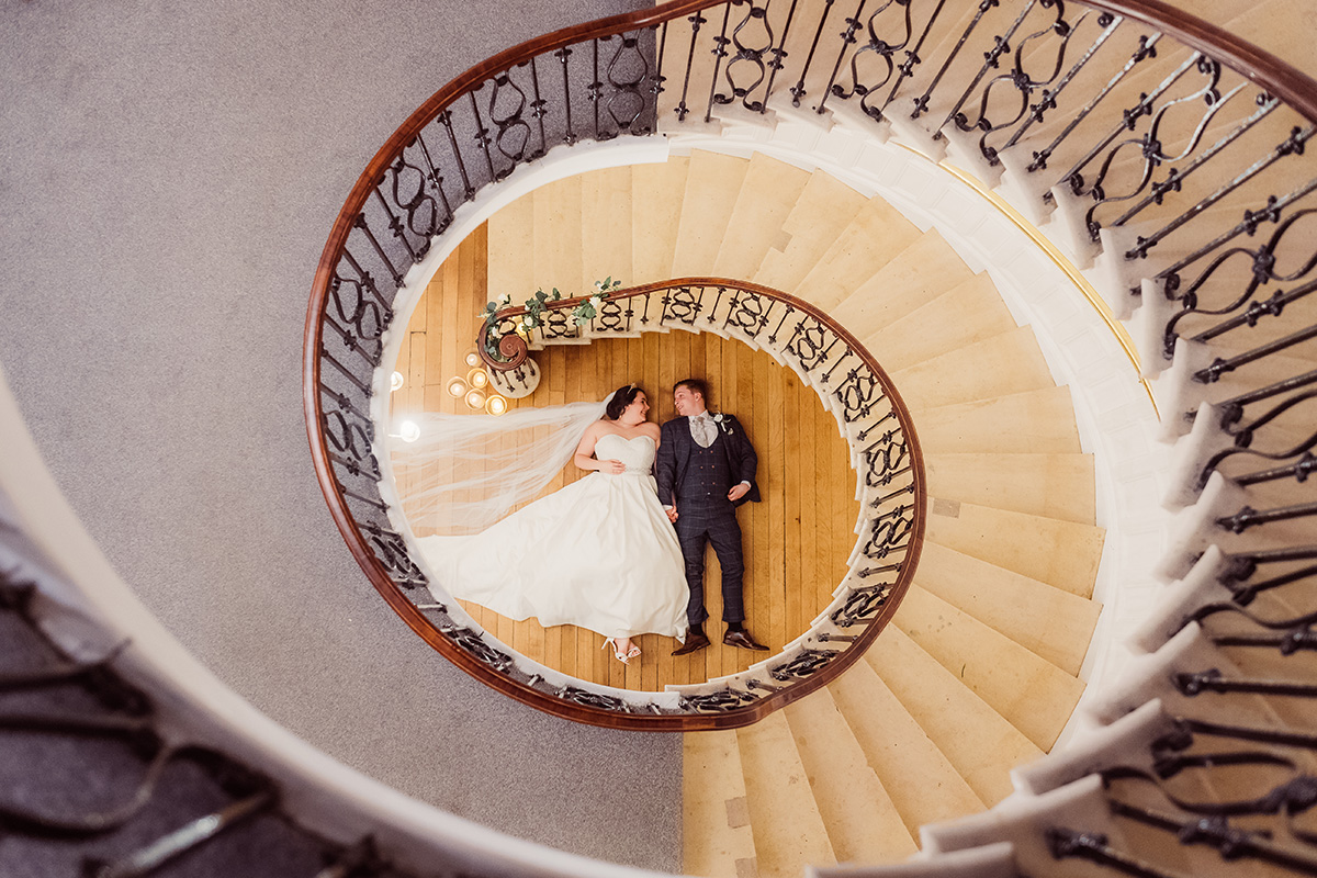 Bride and groom on a floor below a beautiful staircase