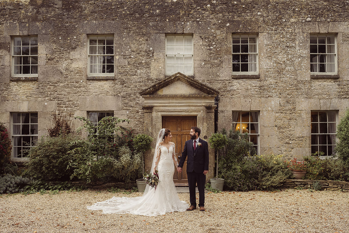 Bride and groom standing outside a cotswold stone house