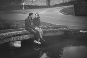 Engaged couple sitting by a stream chatting and holding hands